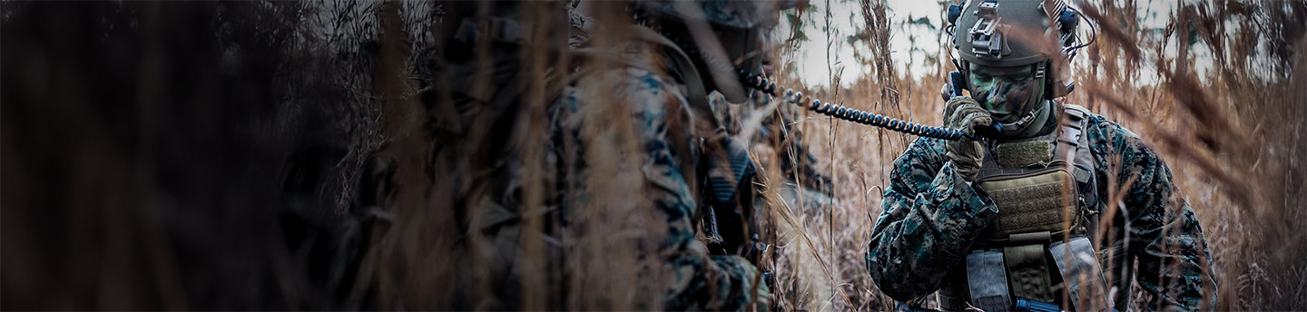 Marines with tactical gear and communications equipment conduct operations in tall grass field at Camp Lejeune.